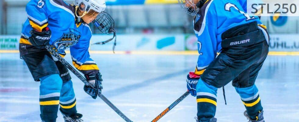 Two young athletes face-off during an ice hockey game in an indoor rink.