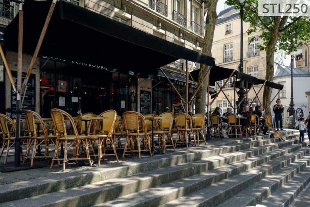 Outdoor Paris café with wicker chairs and people enjoying a sunny day on stone steps.