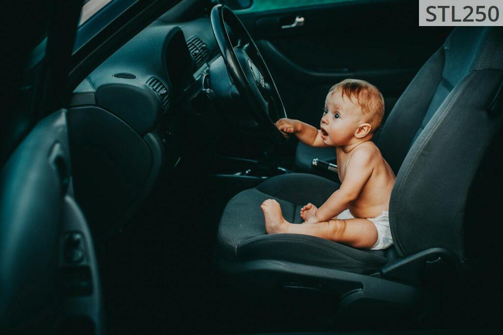 Cute baby sitting on the driver's seat of a car, looking curious and playful.
